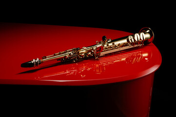 Straight Soprano saxophone on the surface of a red piano. Shallow depth of field.  - obrazy, fototapety, plakaty