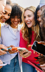 Happy female group using mobile phone together outdoors. Diverse women friends laughing while watching funny social media content on cellphone network app. Friendship and technology lifestyle concept - obrazy, fototapety, plakaty