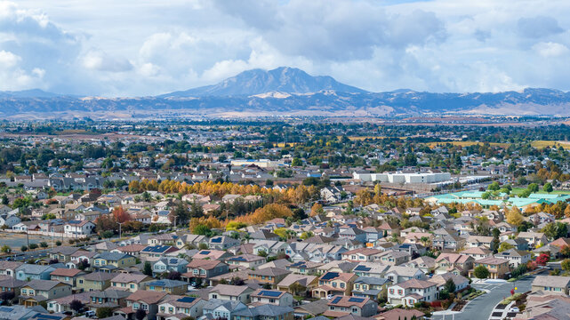 A drone telephoto photo of a community in northern California with a large mountain in the background with a clouded sky
