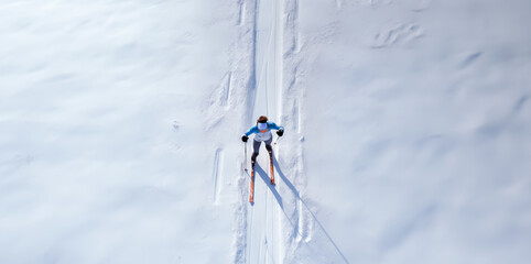 Cross country skier skiing through a snow covered path in the woods on a sunny winters day. Aerial view or top down. Shallow field of view.