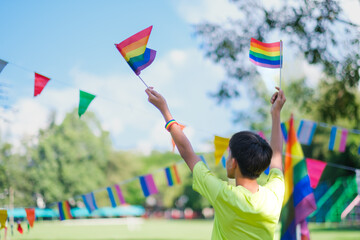 LGBTQ community celebration pride month, young asian kid holding flags facing backwards with nature...