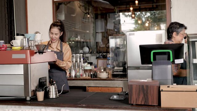 Asian barista female and retirement 60s employee wearing apron uniform open cafe bakery shop small business owner making hot coffee from professional machine, elderly woman serves coffee to customers