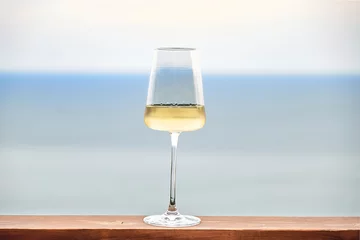 Foto op Canvas White wine in glass against a background of blue sky and sea. Front view. Copy Space. © Alisa Chikov