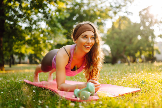 Young woman doing yoga, stretching in the park. Beautiful woman in sportswear is training outdoors. Fitness, sport concept.