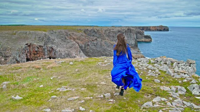 Tourist girl standing on a cliff enjoying the view of the Pembrokeshire Coast National Park. A beautiful woman enjoying turquoise water coastal walks, watersports, scenic beaches and coves in Wales.