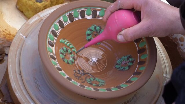 Close up real time shot of hands painting  ukrainian pattern on glased  clay plate.