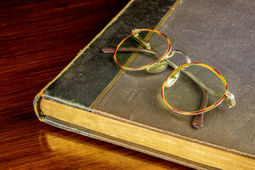 Old Book and Spectacles on a Polished Wooden Table Top - 674834424