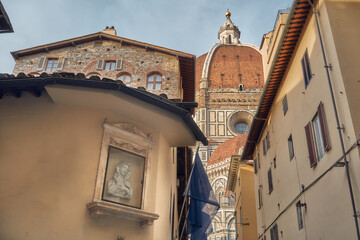 Brunelleschi's dome of the cathedral of Santa Maria del Fiore in Florence seen from a small street, on the left a shrine of the Virgin Mary