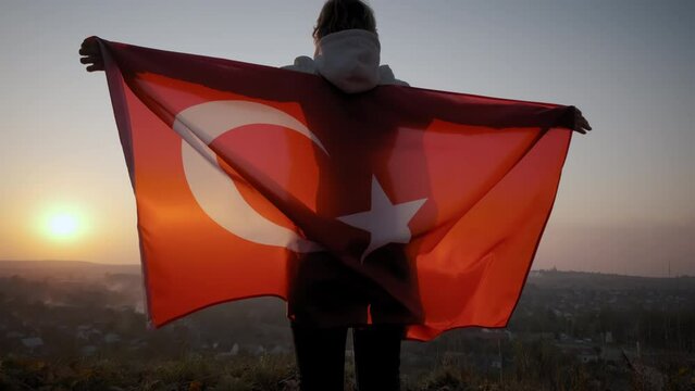 Back view of happy woman with turkish national flag standing outdoors at sunset. Wide footage