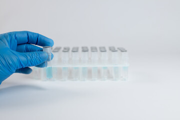 Hand in blue glove demonstrates test tube for analysis. Test tubes in stand