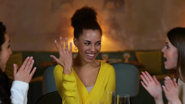 Happy African American woman resting with friends in the restaurant while showing her wedding ring to them. Lifestyle, friendship concept. Real time video.