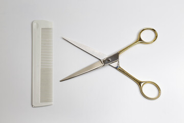 Golden scissors and plastic comb on a white background. Beauty, fashion, haircut, style concept.