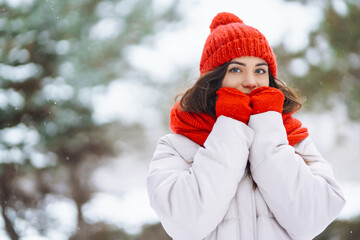 Obraz premium Portrait of a beautiful woman in a red hat in a snowy forest. Young woman having fun with snow on a winter day. Vacation concept, nature.