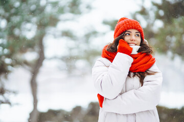 Portrait of a beautiful woman in a red hat in a snowy forest. Young woman having fun with snow on a winter day. Vacation concept, nature.