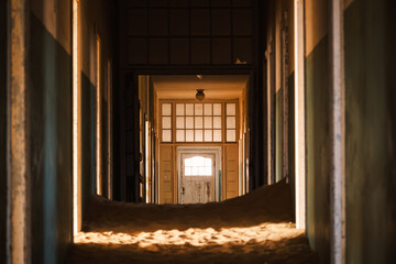 Interior of the abandoned hospital in Kolmanskop, Namibia, engulfed by sand and lit up by the warm...