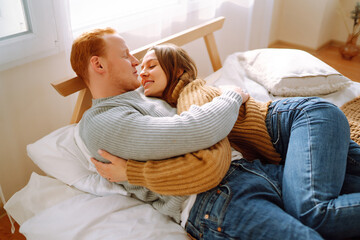 Beautiful young couple at home. A couple in love is relaxing on the bed at home, hugging each other, giving gifts and having fun. Holiday concept, time together.
