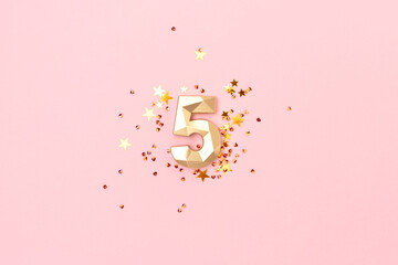 Golden number five and stars confetti on a pink background. Festive creative concept.