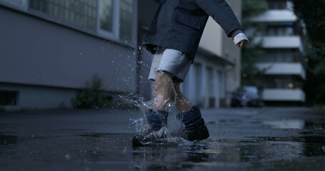 Nostalgic scene of child kicking puddle of water in street alley having fun by himself filmed in...