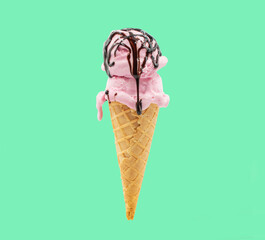 A wafer cone with strawberry ice cream and chocolate syrup with a green background 