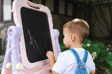 A little boy that is standing in front of a chalkboard. A Curious Little Boy Captivated by the Chalkboard Magic