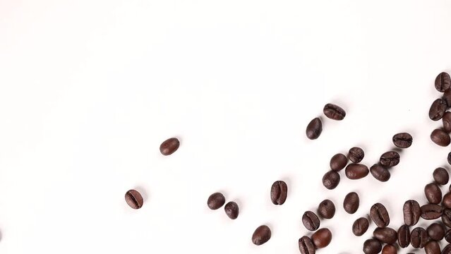 Video footage of coffee beans splashing from the corner of a photo on a white background.
