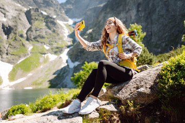 Happy female traveler with a yellow backpack and a phone in her hands takes a selfie and blogs...