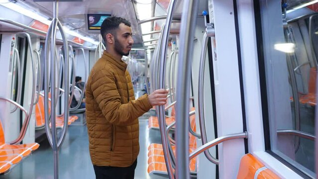 portrait of young pensive migrant holding at the grab bar on the metro train