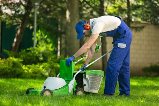 Professional garden worker, working with electric lawn mower on grass