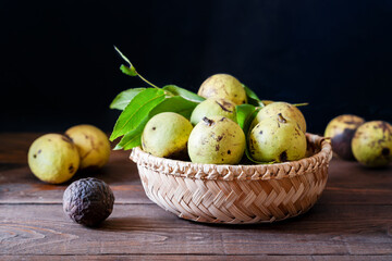 Group of black walnuts or jugulars nigra in a basket with leaves on wooden table. Dark mood style of shooting