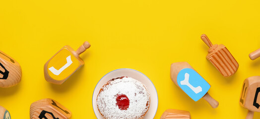 Dreidels and tasty donut for Hanukkah celebration on yellow background, top view