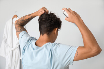 Handsome young man with tattoo applying hair spray on his curly hair in bathroom