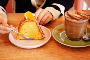 Woman enjoying pumpkin chai while eating orange cake at a cafe