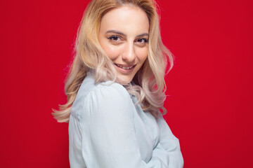 Face of nice girl keeps chin on shoulder, isolated on red background. Closeup portrait of a cheerful woman