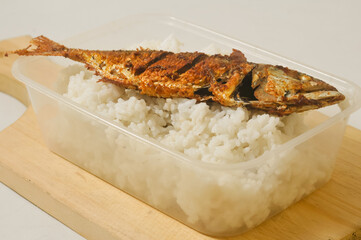 White rice and a fried fish served in a plastic box on a wooden cutting board isolated on a white background