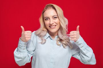 Young woman with thumbs up, like concept, isolated on red background. Yes gesturing, sings of good work