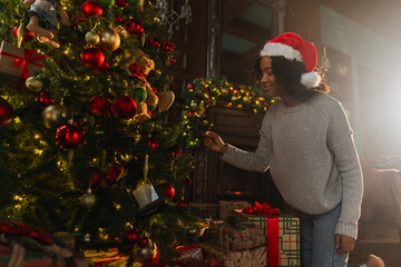 Merry Christmas. African American woman decorating Christmas tree. Happy girl near traditional...