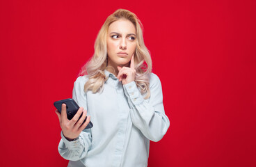 Consider trendy girl browse on mobile phone, isolated on red background. Young woman holding mobile phone and thinking