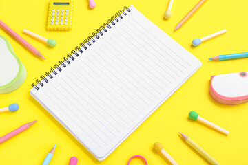 Notebook with different stationery supplies on yellow background
