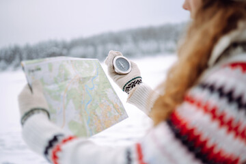 Curly-haired young woman standing in the wild with a map and compass in a snowy forest. Winter is...