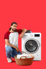 Young man with laundry basket near washing machine on red background
