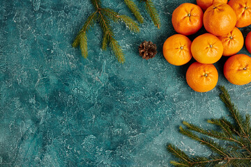 ripe mandarins and fir branches with pine cone on blue textured background with copy space