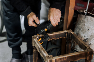 An adult male professional woodworker, carpenter, worker glues a chair, repairs, restores furniture...