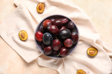 Bowl with fresh ripe plums on light background