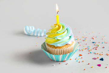 Delicious birthday cupcake with burning candle on grey background