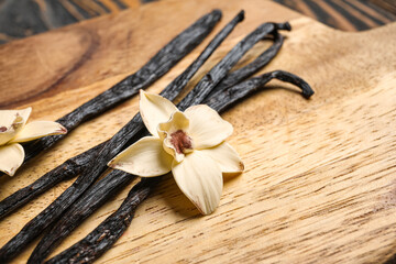 Wooden board with aromatic vanilla sticks and flowers, closeup