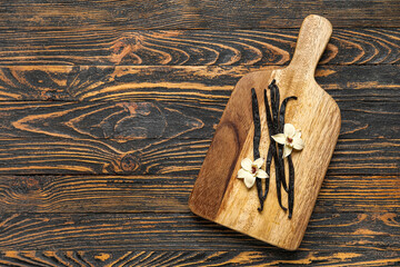 Board with aromatic vanilla sticks and flowers on black wooden background