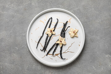 Plate with aromatic vanilla sticks and flowers on grey background