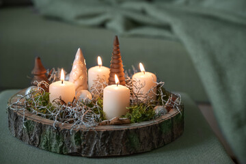 Christmas decoration and white advent candles and on a rustic tree tray on an gray green ottoman by...
