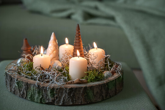 Christmas decoration and white advent candles and on a rustic tree tray on an gray green ottoman by a couch with a blanket, cozy home decor, copy space, selected focus