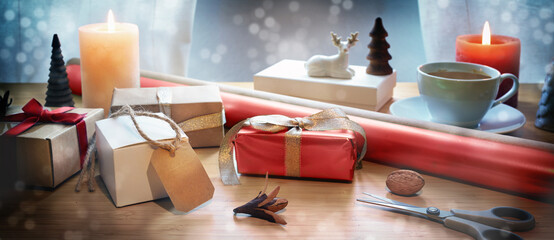 Holiday gift wrapping on a table with present boxes, scissors, red paper, candles and Christmas...